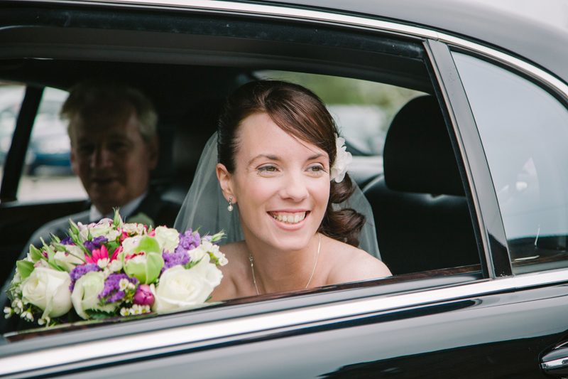 Bride looking out of car window with dad next to her